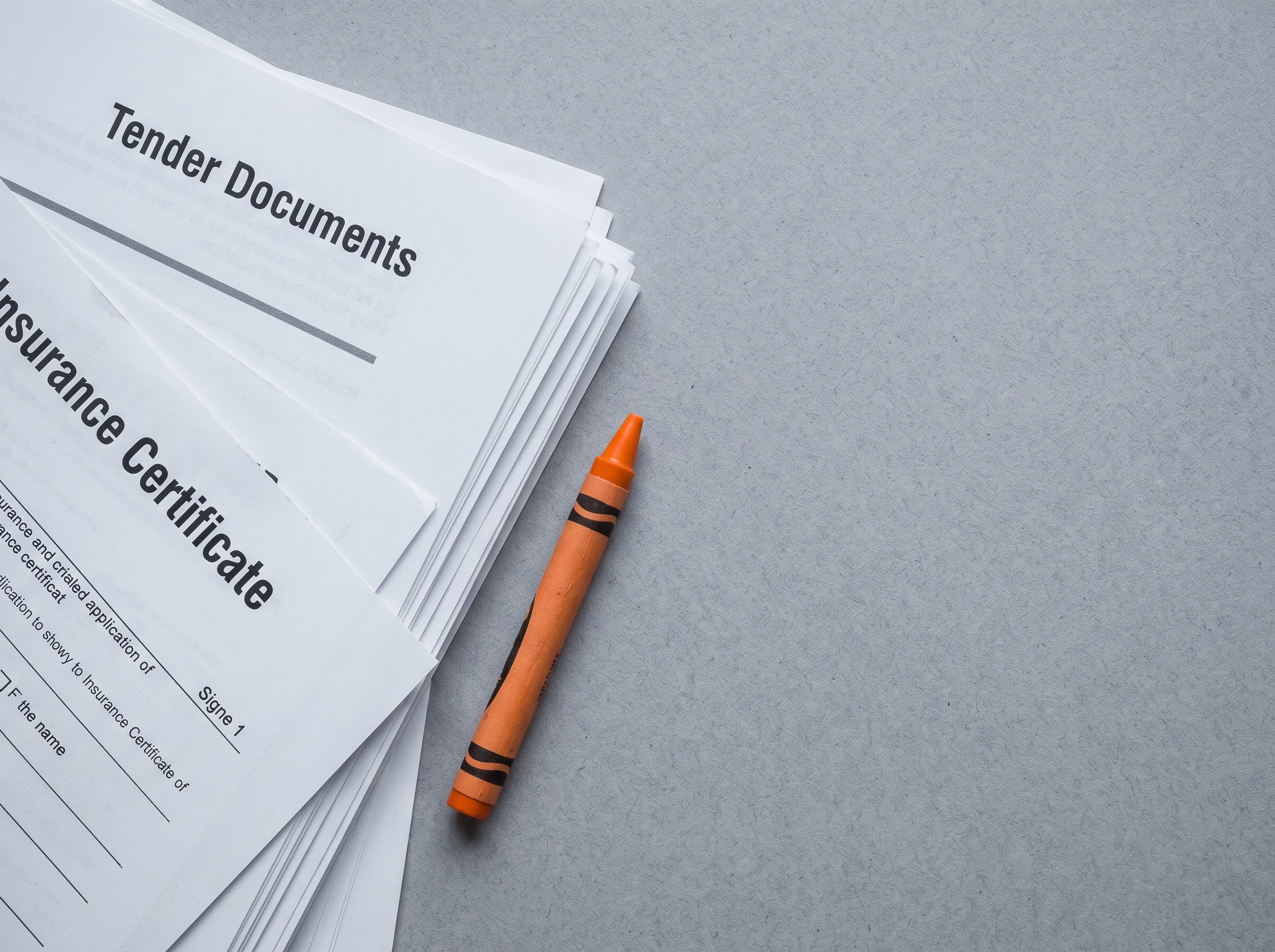 A flat-lay of bound method statements, an insurance certificate and an orange crayon on grey report paper